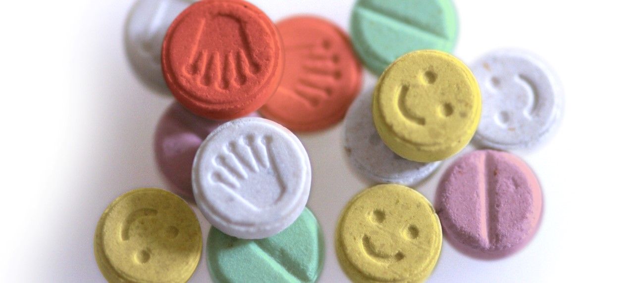 Colorful round tablets with hand and smiley face imprints, scattered on white surface